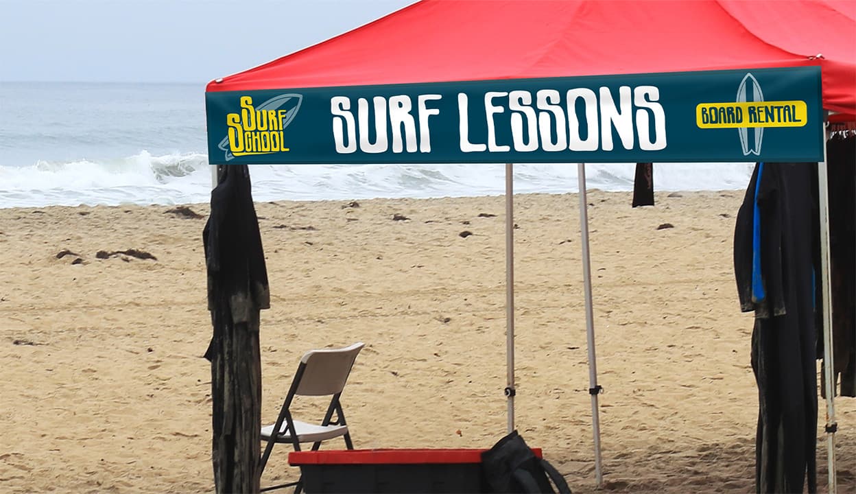 canopy tent banner advertising surf lessons on the beach