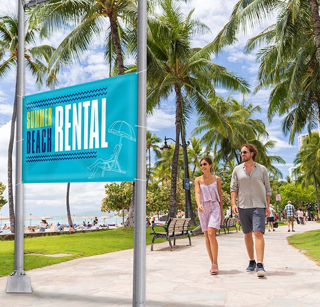 people walking and seeing a double sided banner outside at the beach that is advertising beach rentals
