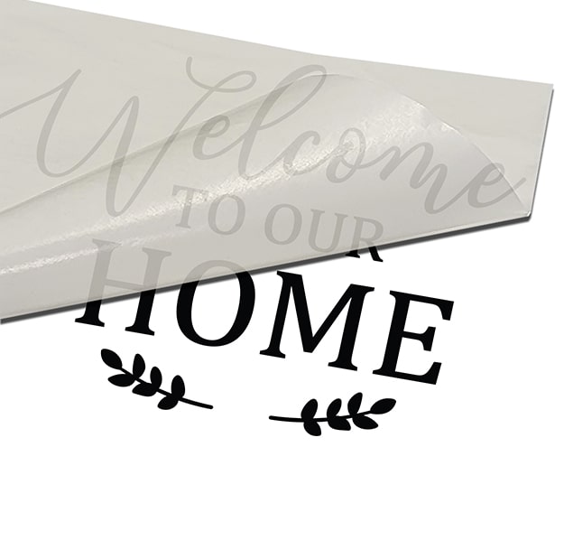 black welcome home wall quote being installed on a white surface and transfer tape being peeled off at an angle from the bottom towards the top of the graphic